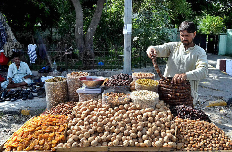 A vendor arranging and displaying the different kinds of Dry fruits to the customers on their handcart at roadside