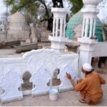 An artisan is painting the minarets used in the decoration of the mosque at his workplace
