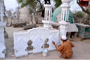 An artisan is painting the minarets used in the decoration of the mosque at his workplace