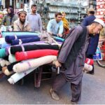 Worker on hand cart carrying clothes to shift shop at Masjid Road