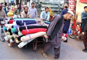 Worker on hand cart carrying clothes to shift shop at Masjid Road