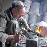 An old blacksmith busy in preparing saw at his work place for upcoming winter season to cut fire woods