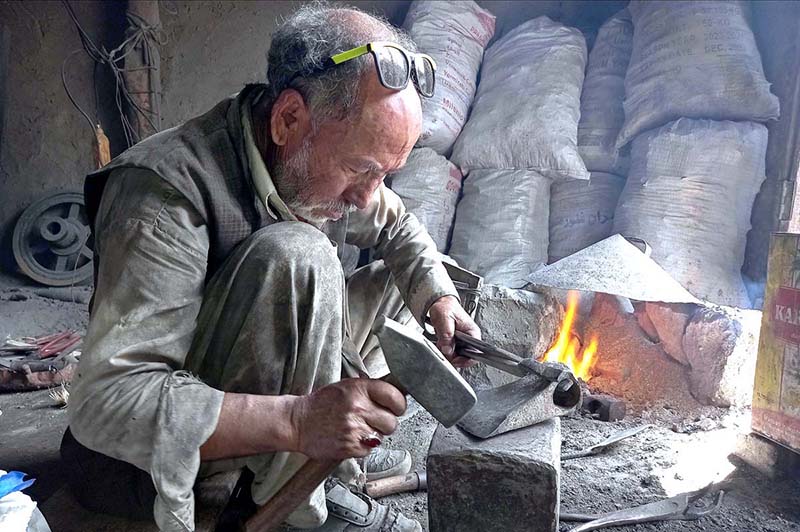 An old blacksmith busy in preparing saw at his work place for upcoming winter season to cut fire woods