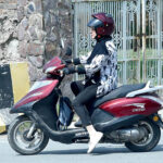 A woman is riding a scooter on her way to her destination.