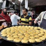 A vendor is busy in making and selling the traditional food item “Laddu Peethi” to the customers at outside Dehli Gate.
