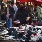 A lady selecting and purchasing second hand shoes at a vendors setup in Landa Bazar