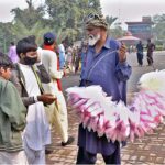 An elderly vendor selling cotton candy (Lacha) while shuttling on road.