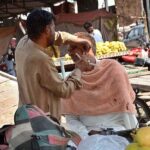 A barber shaving of a costumer at his roadside setup