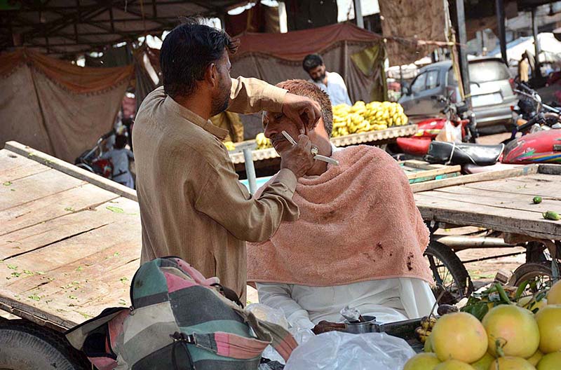 A barber shaving of a costumer at his roadside setup