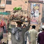 A vendor carrying cage on his head with hens for selling while shuttling on road in a local market.