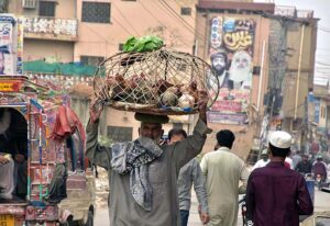 A vendor carrying cage on his head with hens for selling while shuttling on road in a local market.