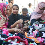 Women selecting and purchasing old warm clothes from vendor at cloth market road