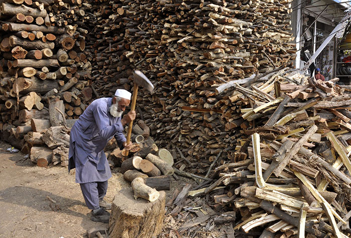 Old man cutting wood into pieces for selling purpose at his workplace in the Federal Capital.