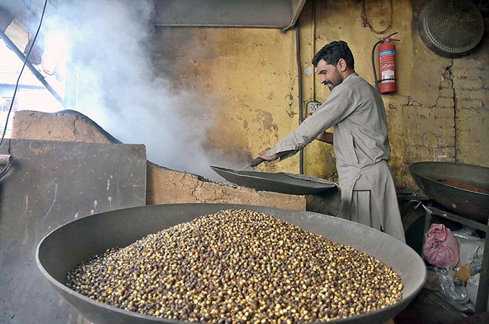 A worker busy in roasting grams at his workplace in local market.