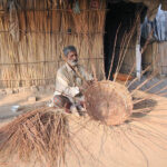 An aged person preparing a basket with dry branches of the tree to sell for livelihood outside his makeshift home