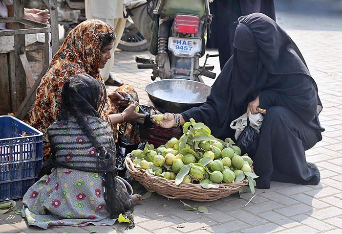 A woman purchasing guavas from roadside woman vendor