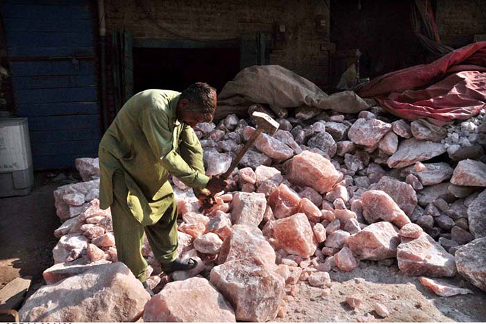 A worker busy in breaking pink salt into pieces at his workplace.