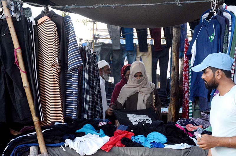 A woman selecting to purchase used clothes from a set-up by vendor in Saddar area