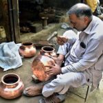 Artisan making old-fashioned brass vessels at his setup.