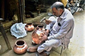 Artisan making old-fashioned brass vessels at his setup.
