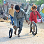 Gypsy children playing with tire on the road at Latifabad.