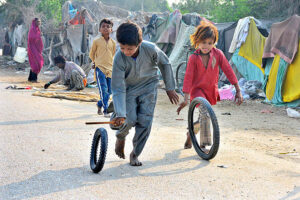 Gypsy children playing with tire on the road at Latifabad.