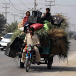 A family traveling on tricycle rickshaw loaded with fodder heading towards their destination at autobahn road.