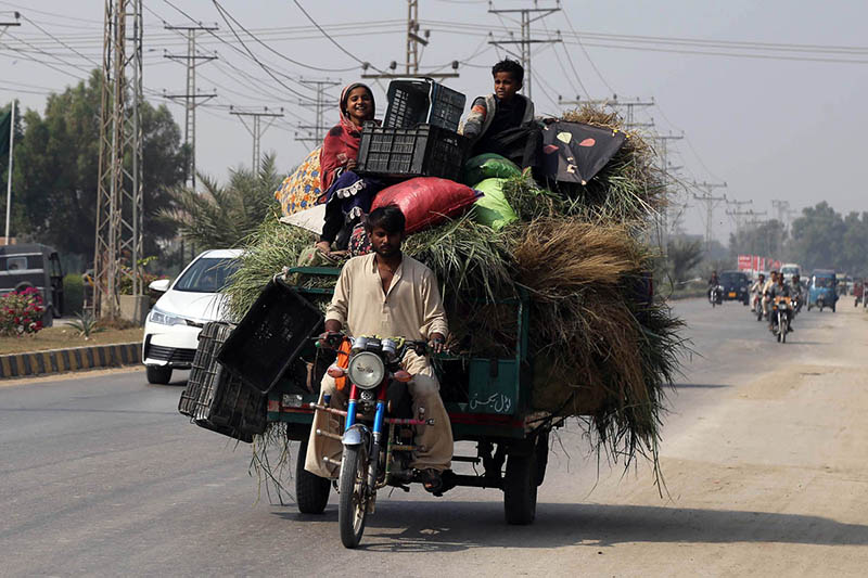 A family traveling on tricycle rickshaw loaded with fodder heading towards their destination at autobahn road.