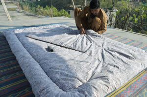A worker stitches quilt as per increasing demand of customers at his workplace.