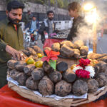 A vendor displays charcoal-roasted sweet potatoes to attract customers at his roadside setup.