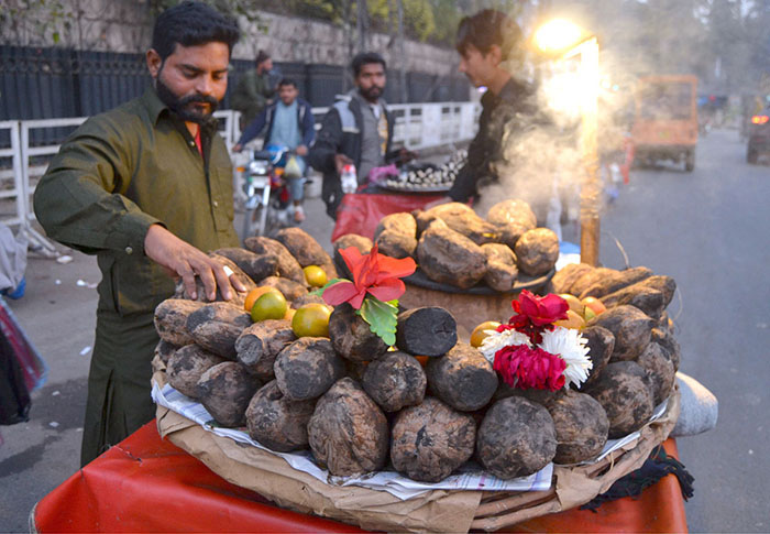 A vendor displays charcoal-roasted sweet potatoes to attract customers at his roadside setup.