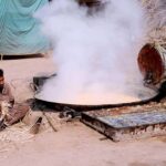 A worker boiling sugar cane extract to make traditional sweet item (Gurr) at his workplace.