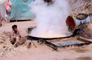  A worker boiling sugar cane extract to make traditional sweet item (Gurr) at his workplace.