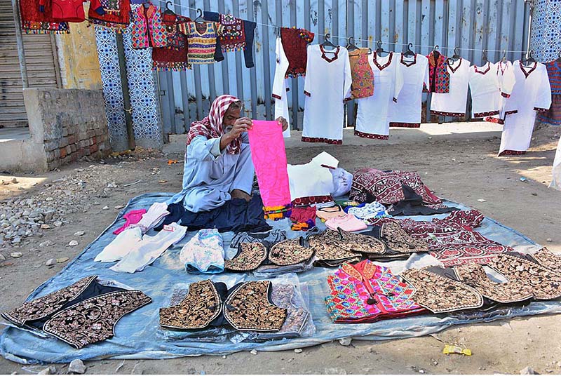 An elderly vendor displaying the Sindhi cultural dresses to attract the customers at roadside