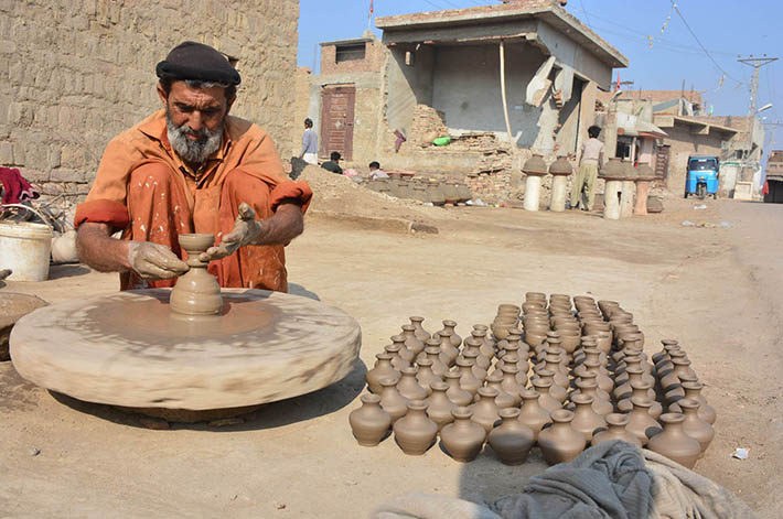 An elderly worker busy in preparing clay-made lamp at his workplace.