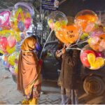 Young street vendor displaying the lighting balloons to attract the customers at Latifabad
