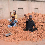 Labourers crushing bricks into pieces for construction use.