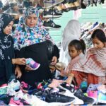 Women selecting and purchasing second hand shoes from vendor at Station road