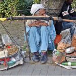 An elderly man waiting for costumers sitting on the roadside