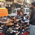 Customers selecting and purchasing shoes from roadside vendor at Qissa Khawani Bazar