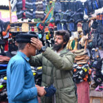 A vendor displaying and selling warm cap to customer during winter season at Bacha Khan Chowk