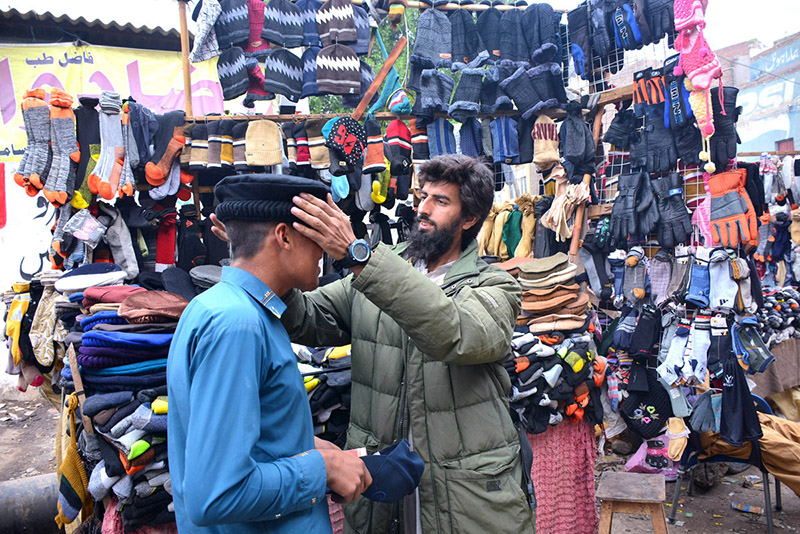 A vendor displaying and selling warm cap to customer during winter season at Bacha Khan Chowk