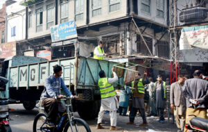 Municipal Corporation staff are picking up the illegal encroachments in Jhang Bazar and loading them into the vehicle. 