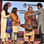 Group photo of Federal Minister Madad Ali Sindhi receiving a Sindhi Ajrak from the organizer during the Sindhi Cultural Day event organized by Soormiyun at PNCA