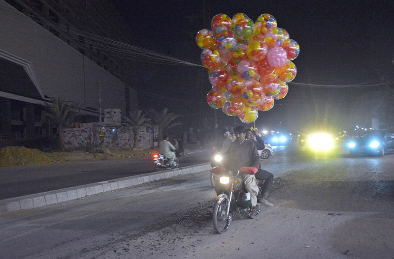 Vendor carrying colourful balloons on motorbike rear seat passing through Korangi road