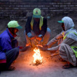 Employees of Sindh Solid Waste Management Board (SSWMB) sitting around the fire to keep them warm in a chilled weather during morning time