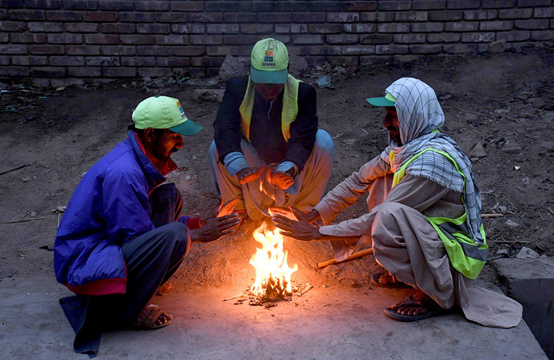 Employees of Sindh Solid Waste Management Board (SSWMB) sitting around the fire to keep them warm in a chilled weather during morning time