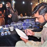 A man busy in work on blue potry stalls during Lok Mela organized by Parks and Horticulture Authority