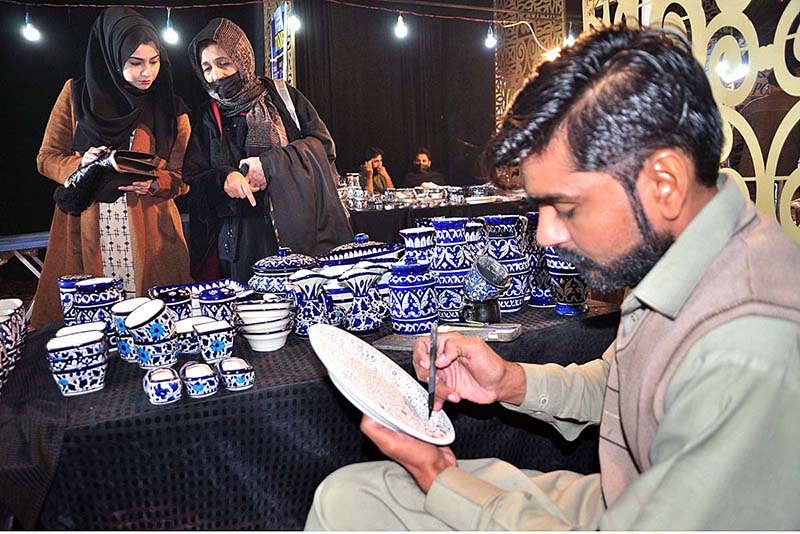 A man busy in work on blue potry stalls during Lok Mela organized by Parks and Horticulture Authority