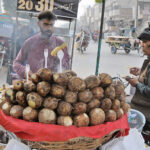 A vendor selling charcoal-roasted sweet potatoes to attract customers at his roadside setup